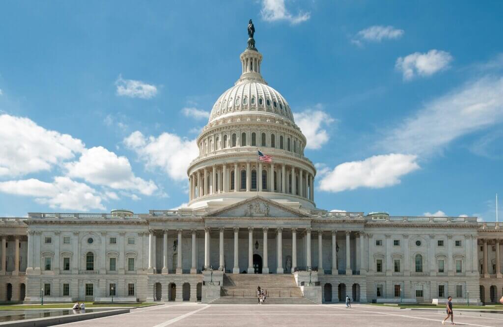 United States Capitol building with American flag and people on steps under blue sky