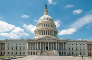 United States Capitol building with American flag and people on steps under blue sky