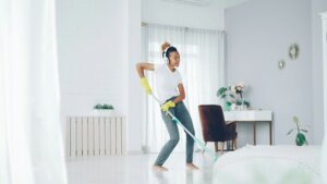 Woman wearing headphones and yellow gloves dancing while mopping the floor in a bright living room