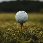 Titleist golf ball on a wooden tee in grass with blurred background