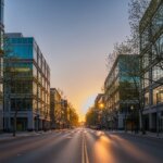 Empty city street at sunset with modern glass office buildings and trees lining both sides.