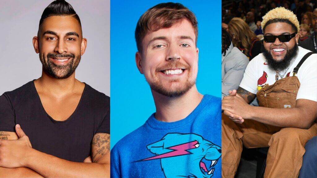 Three smiling men, one in a black shirt with tattoos, one in a blue sweatshirt with a panther graphic, and one in brown overalls and sunglasses at an event