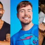 Three smiling men, one in a black shirt with tattoos, one in a blue sweatshirt with a panther graphic, and one in brown overalls and sunglasses at an event