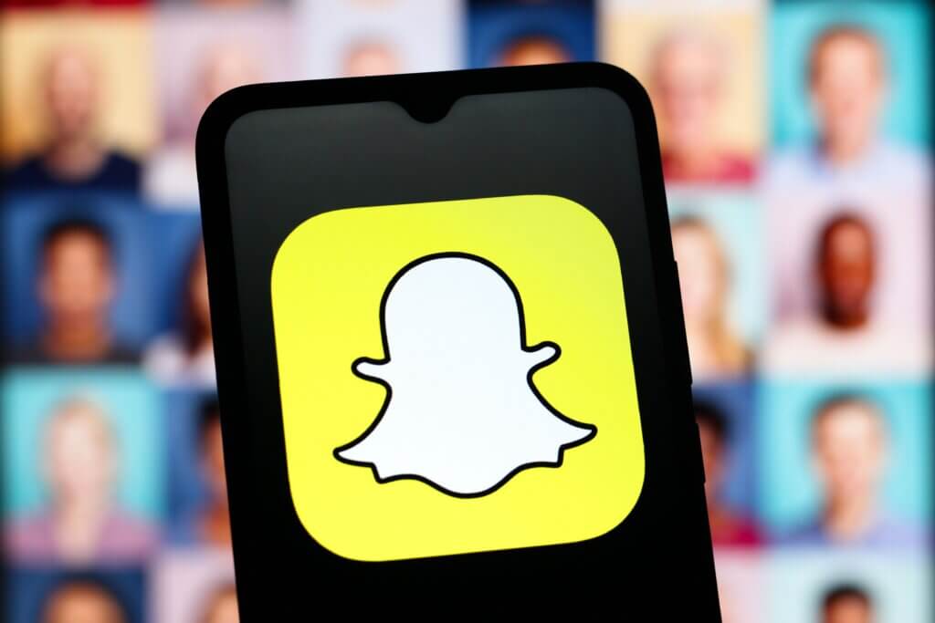 Snapchat app logo displayed on a smartphone screen with blurred faces in the background.