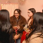 Group of women socializing with cocktails at a Depop event with red ribbon tags on glasses