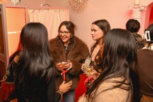 Group of women socializing with cocktails at a Depop event with red ribbon tags on glasses