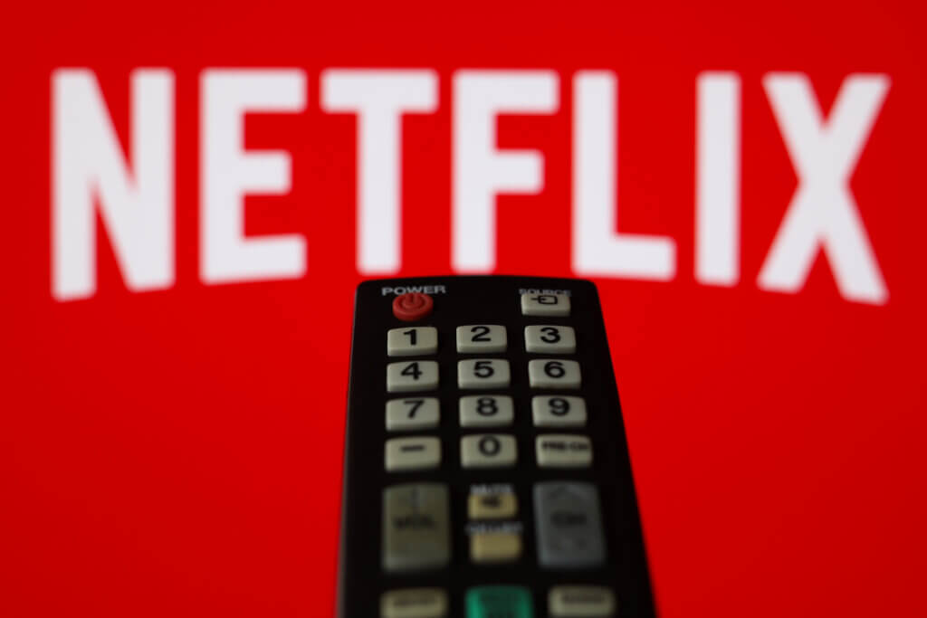 TV remote control in front of a red screen displaying the Netflix logo.