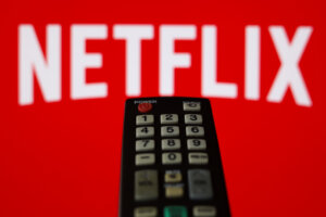 TV remote control in front of a red screen displaying the Netflix logo.
