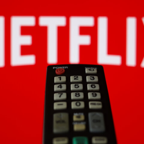 TV remote control in front of a red screen displaying the Netflix logo.