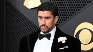 Bad Bunny wearing a black velvet tuxedo with a white flower on the lapel at an awards event.