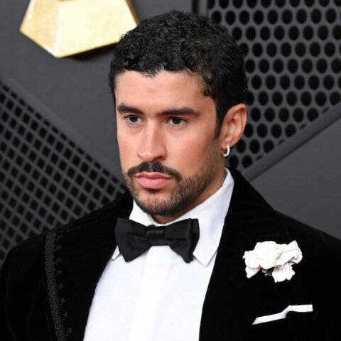 Bad Bunny wearing a black velvet tuxedo with a white flower on the lapel at an awards event.