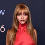 Woman in a red floral embroidered top and red leggings posing at the Best New Artist 2026 event backdrop