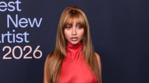 Woman in a red floral embroidered top and red leggings posing at the Best New Artist 2026 event backdrop