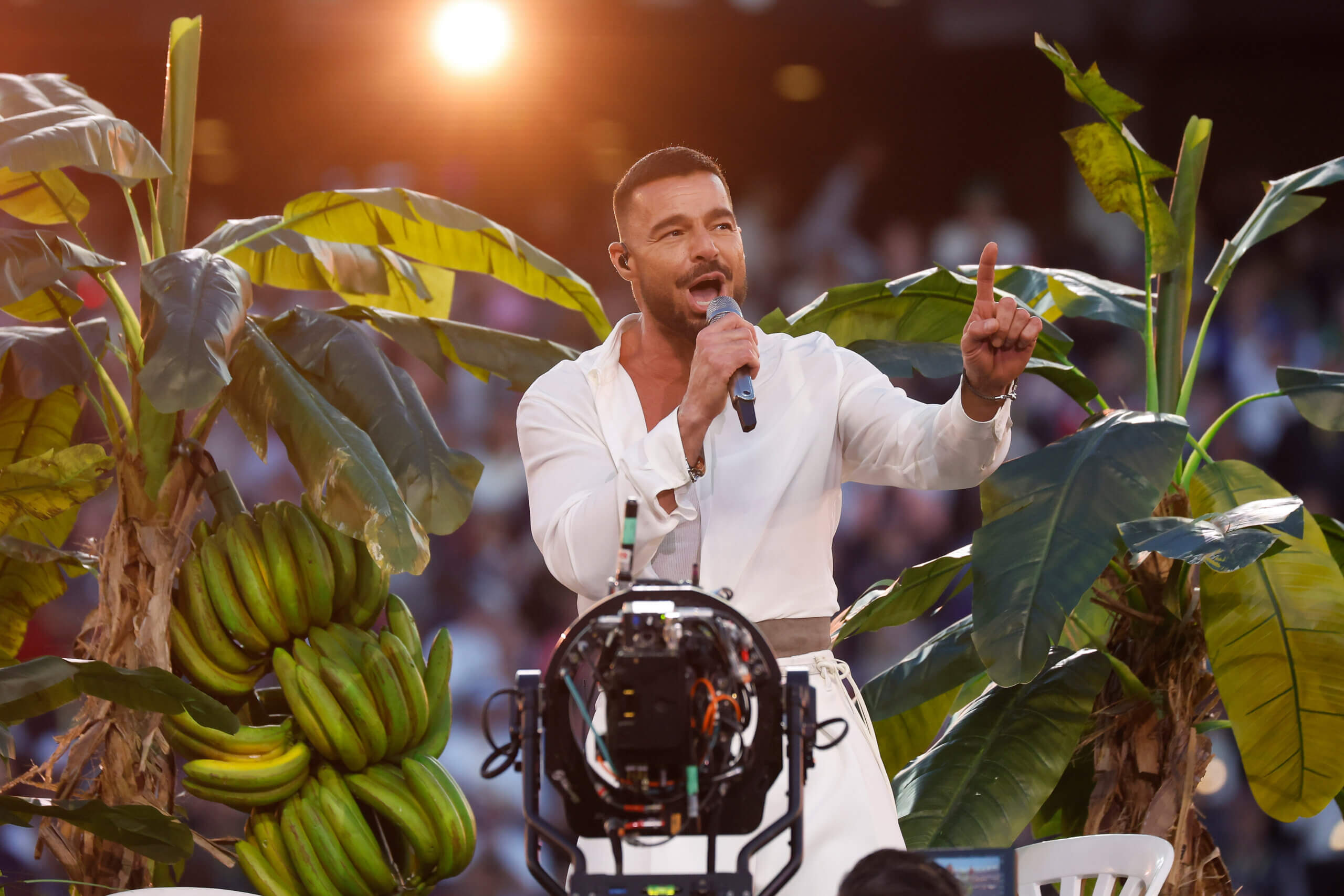 Ricky Martin singing on stage surrounded by banana plants during a live performance.
