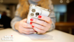 Person with red nail polish holding an iPhone with a clear protective case over a white table