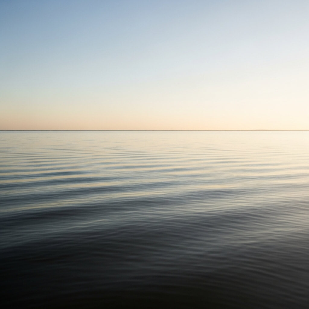 Calm ocean water under a clear sky at sunrise or sunset with gentle ripples on the surface.