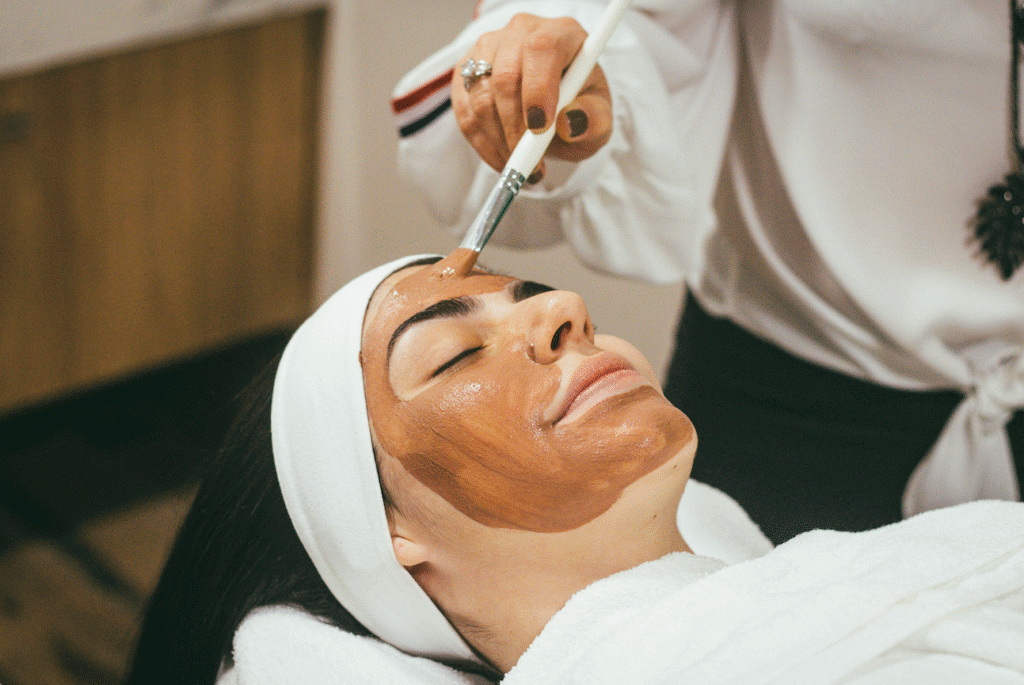 Woman receiving a brown facial mask applied with a brush at a spa or skincare treatment session