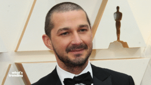 Shia LaBeouf in a black tuxedo with bow tie at an awards event with an Oscar statue in the background