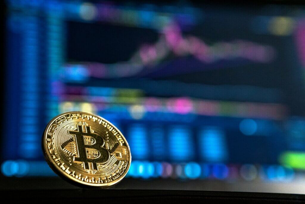 Gold Bitcoin coin with a blurred colorful financial chart in the background