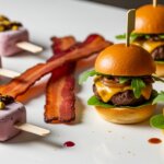 Four mini cheeseburgers with arugula and caramelized onions, two strips of bacon, and three berry popsicles topped with nuts and sauce