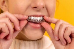 Person inserting a clear dental aligner onto their upper teeth against a yellow background