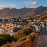 Coastal town with white houses along a beach and mountains in the background at sunset.