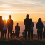 Group of people standing on a hill watching the sunset with a clear sky and distant mountains.