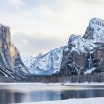 Three people walking near a snowy lake with snow-covered mountains and cliffs in the background at Yosemite National Park.