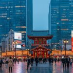 Crowds walking near the illuminated Kanda Myojin Shrine with modern skyscrapers and neon signs in Tokyo at dusk