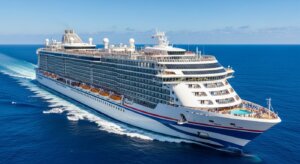 Large white cruise ship with blue and red stripes sailing on clear blue ocean under a sunny sky.