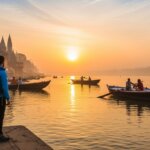 Traveler with backpack standing on riverbank at sunrise with boats and historic temples in Varanasi, India