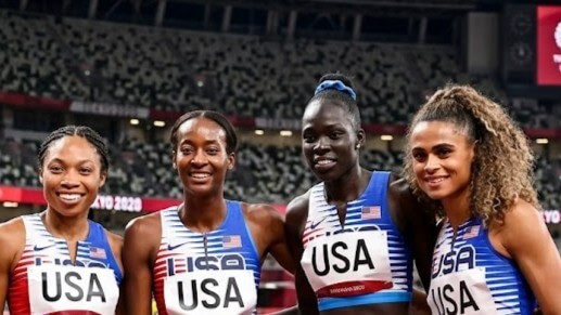 Four female USA track athletes smiling together at Tokyo 2020 Olympics stadium
