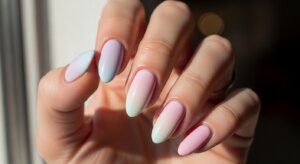 Hand with long almond-shaped nails painted in pastel gradient shades of pink, blue, and white.