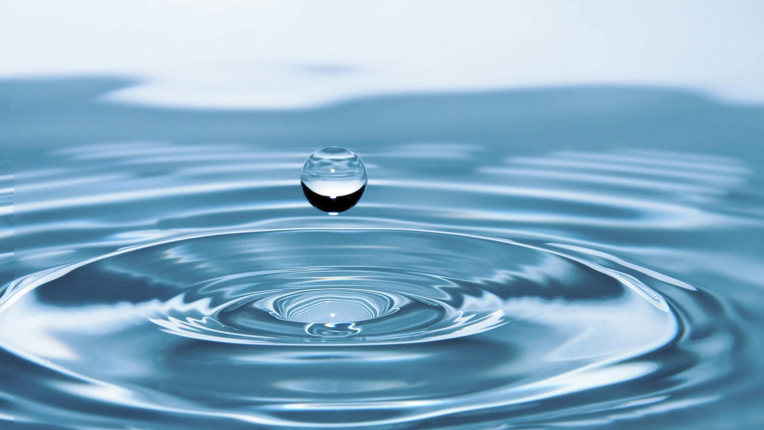 Clear water droplet suspended above rippling water surface with concentric waves