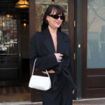 Woman wearing black oversized blazer and sunglasses carrying a white handbag outside a building