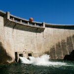 Concrete dam releasing water under a clear blue sky with a basketball digitally added above the dam wall.