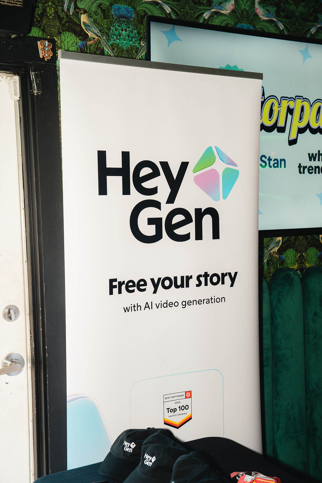 HeyGen banner with slogan "Free your story with AI video generation" and HeyGen branded hats on a table.