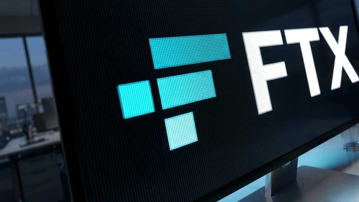 FTX logo displayed on a computer monitor in an office setting at dusk.