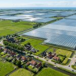 Aerial view of a Dutch village with traditional houses, windmills, canals, and large greenhouse farms.