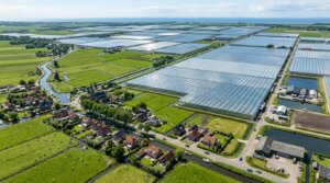 Aerial view of a Dutch village with traditional houses, windmills, canals, and large greenhouse farms.