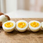 Four halved soft-boiled eggs with partially peeled brown eggshells on a wooden surface