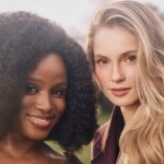 Two women wearing dark purple coats posing outdoors with soft natural light and blurred trees in the background