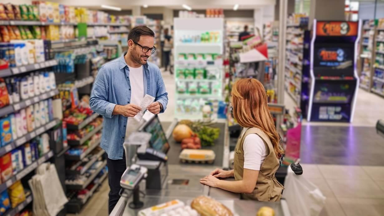 Man holding a receipt talking to a female cashier at a grocery store checkout counter