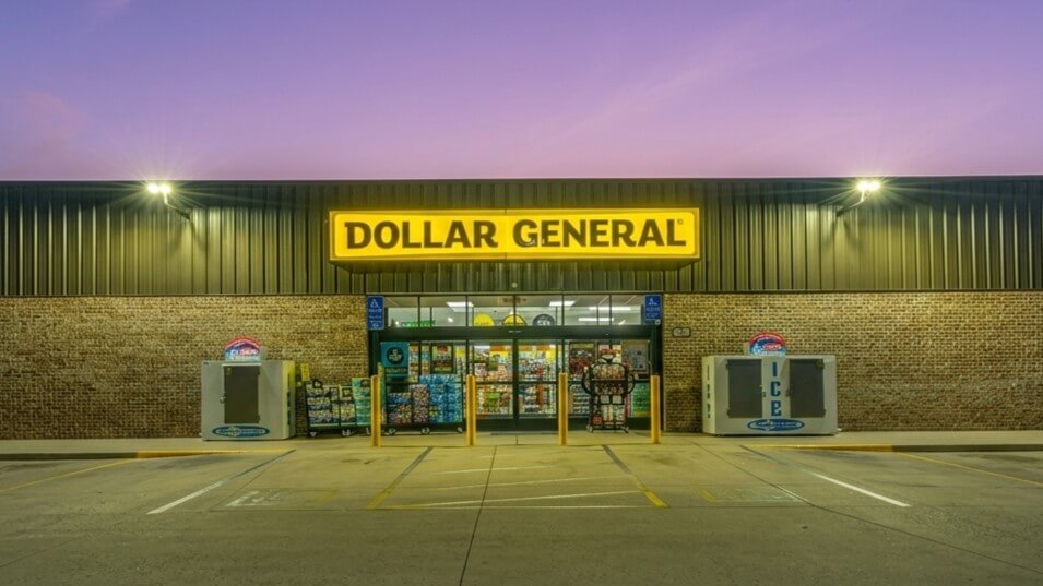 Dollar General store entrance at dusk with illuminated yellow sign and ice vending machines outside.