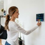 Woman adjusting smart home control panel on wall in modern kitchen