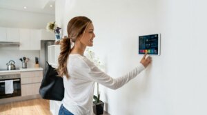 Woman adjusting smart home control panel on wall in modern kitchen