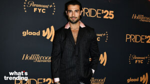 Man in black pinstripe suit with pink collar posing at Paramount+ FYC Pride '25 event backdrop