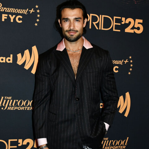 Man in black pinstripe suit with pink collar posing at Paramount+ FYC Pride '25 event backdrop