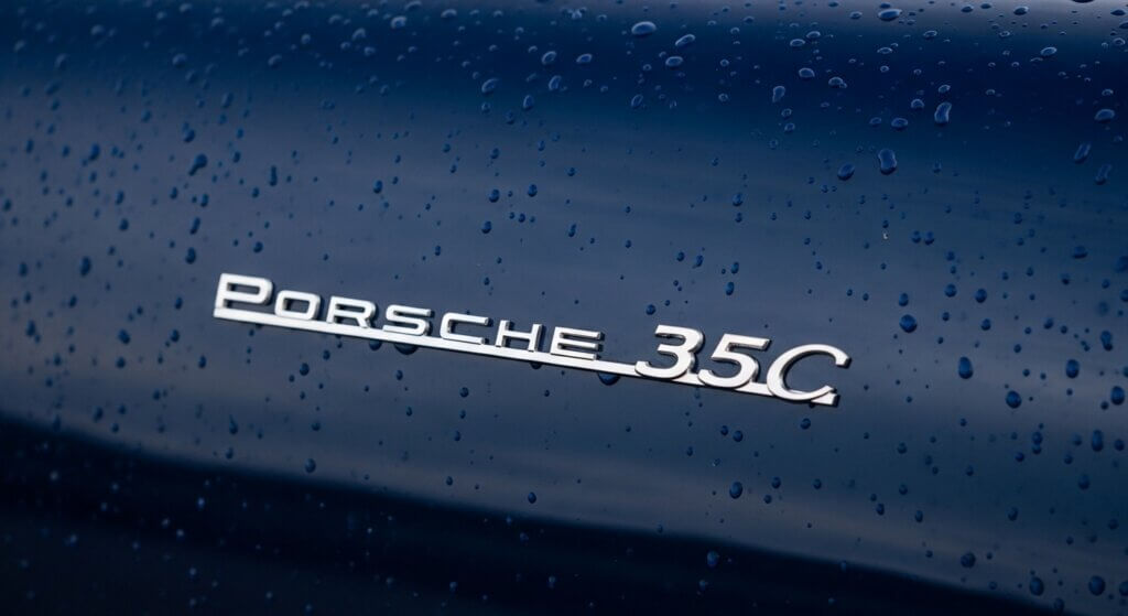 Porsche 356C emblem on dark blue car with water droplets