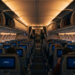 Airplane cabin interior with passengers seated and flight attendants near the front galley.